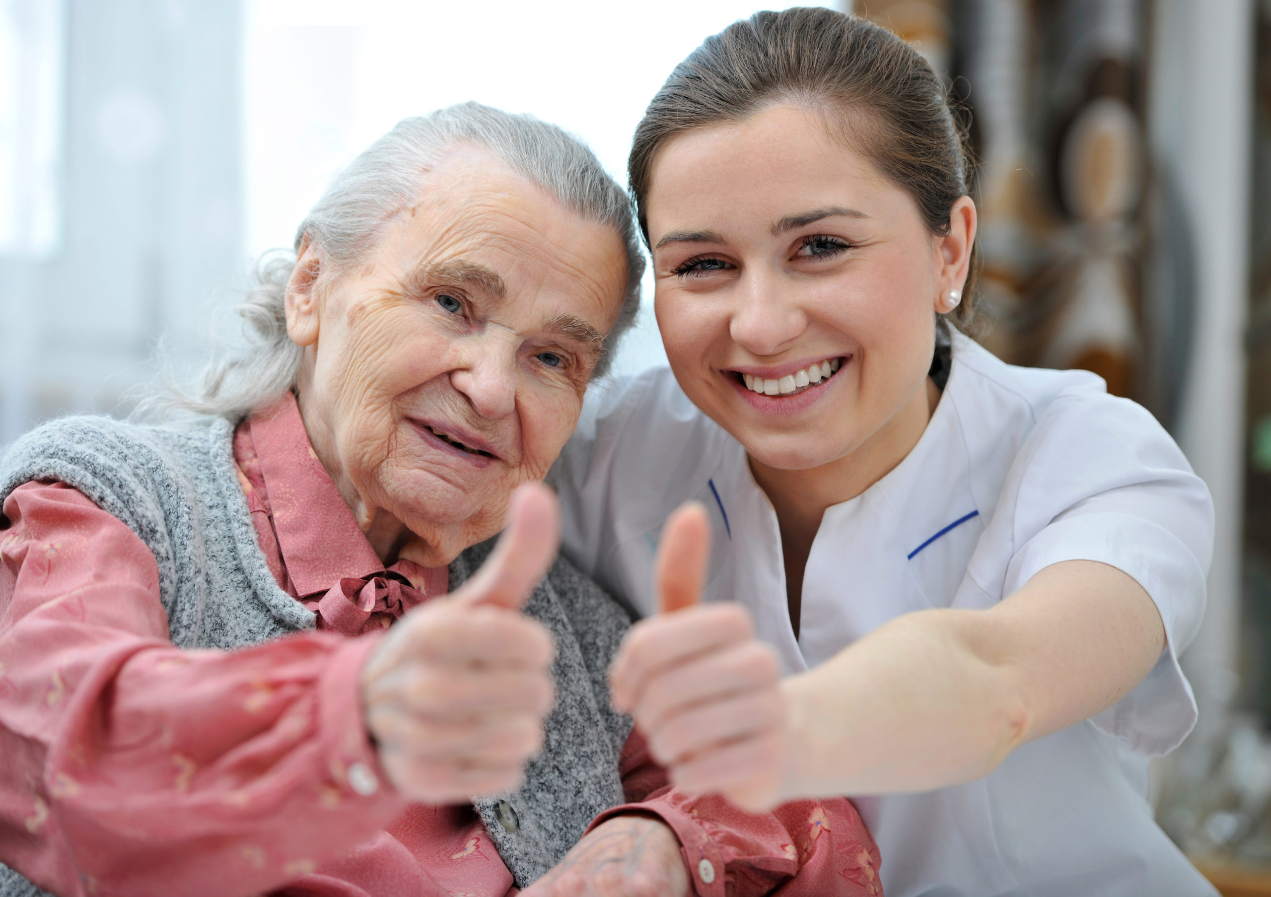 Seniorin und Pflegerin zeigen gemeinsam Daumen hoch