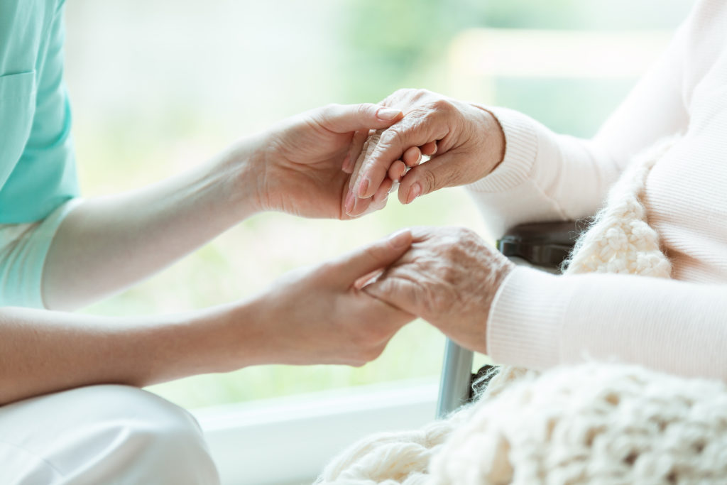 Pflegekraft hält unterstützend die Hände einer Patientin